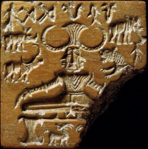 brown seal with carving of a man sitting cross legged. He has 3 faces and a horned like hat. There are lots of animals around him.