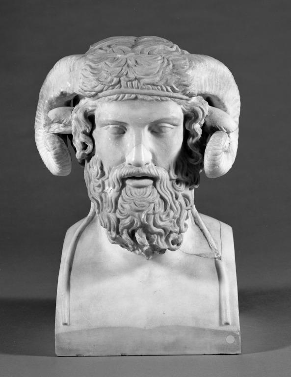 Stone carved into the head of a bearded man with curved horns of a ram.